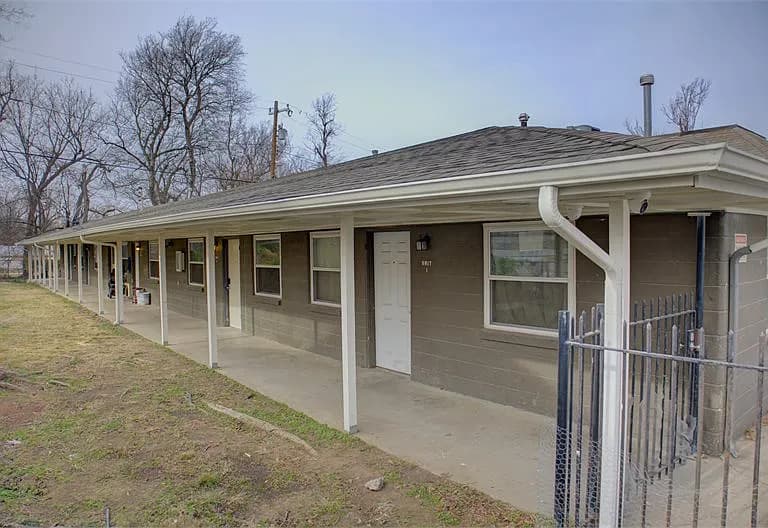 Long gray brick apartment building with a white covered walkway and multiple unit doors.