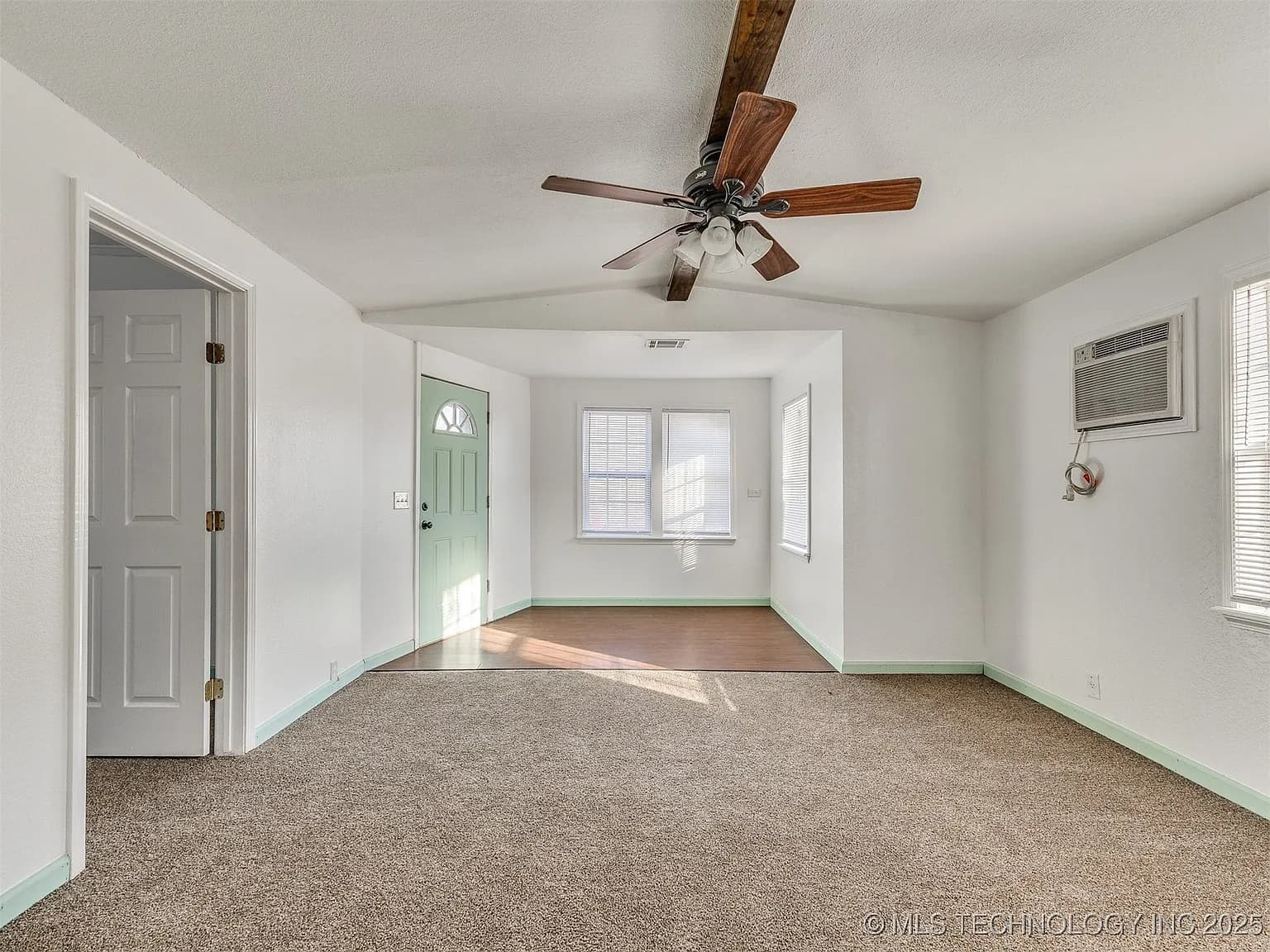 Empty room featuring beige carpet, white walls, light green door, and a wooden ceiling fan.