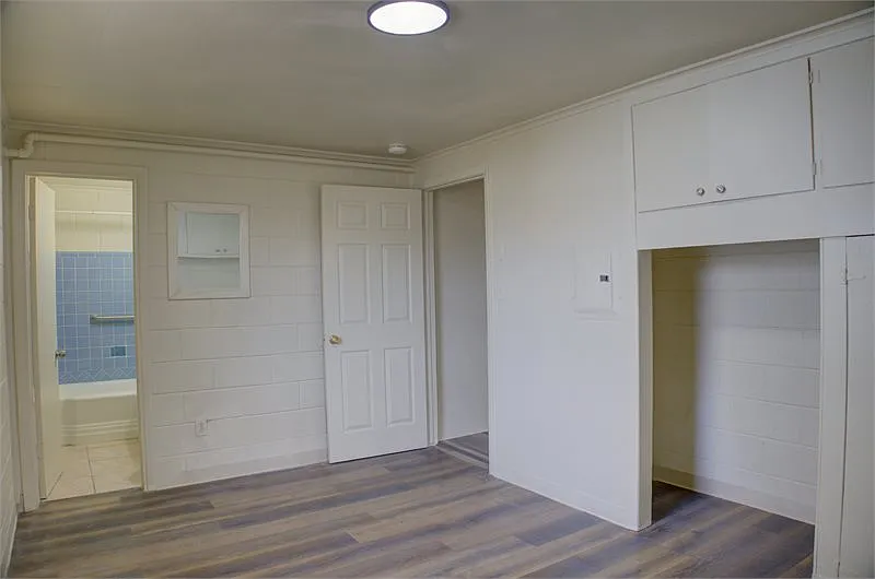 White cinder block room with wood floors, built-in storage, and a blue tiled bathroom.