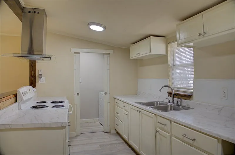 Bright kitchen with white cabinets, marble countertops, electric stove, and a sliding white door.